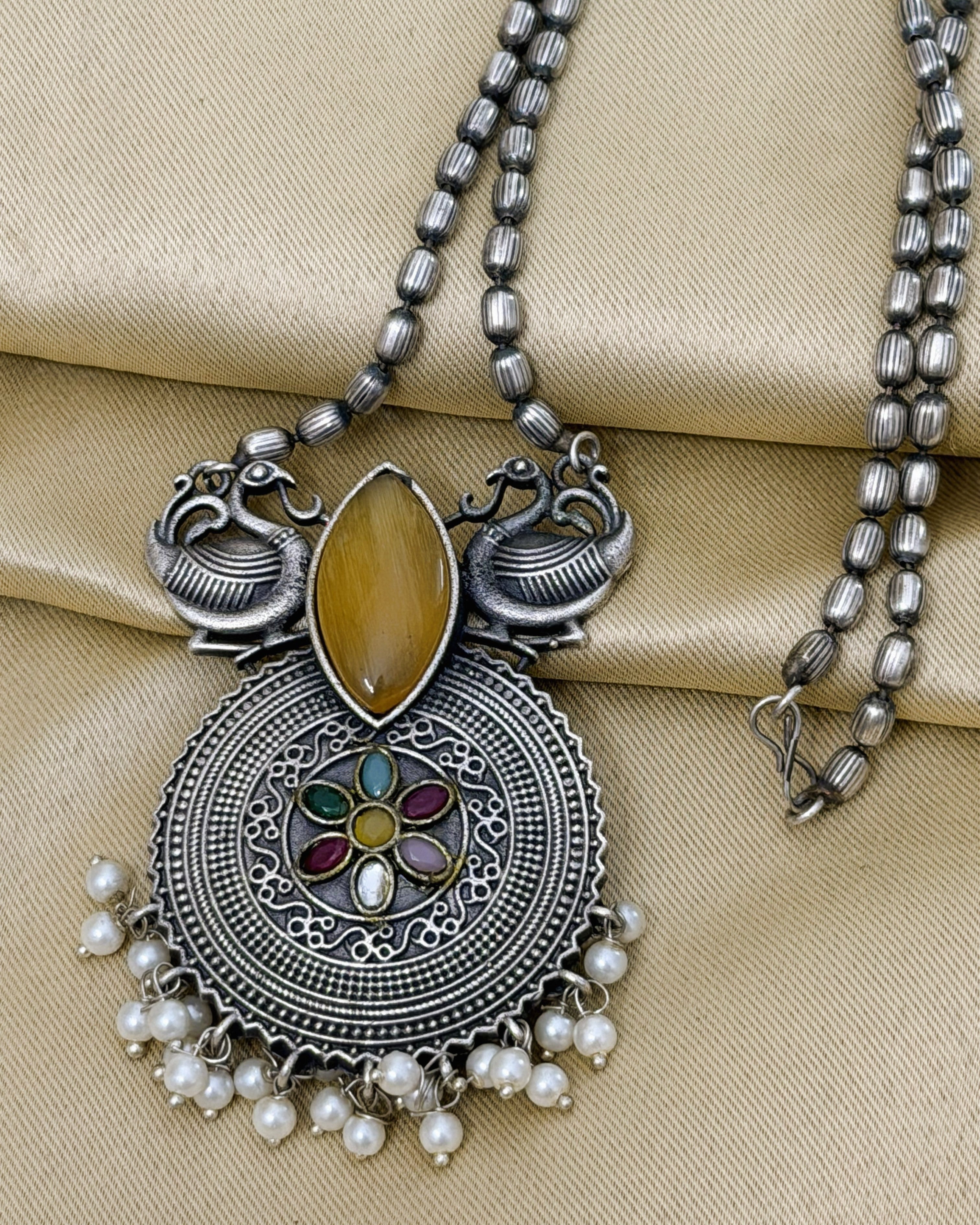 Close-up of antique oxidised pendant with multicolour stones, amber centerpiece and pearl detailing