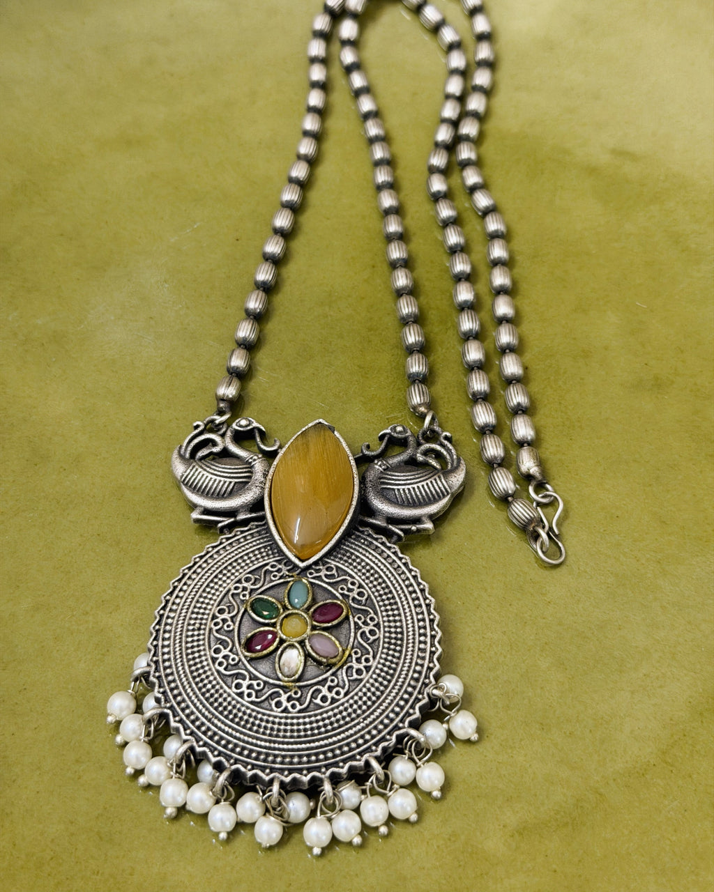 Side angle view of statement necklace highlighting peacock design and textured beaded chain