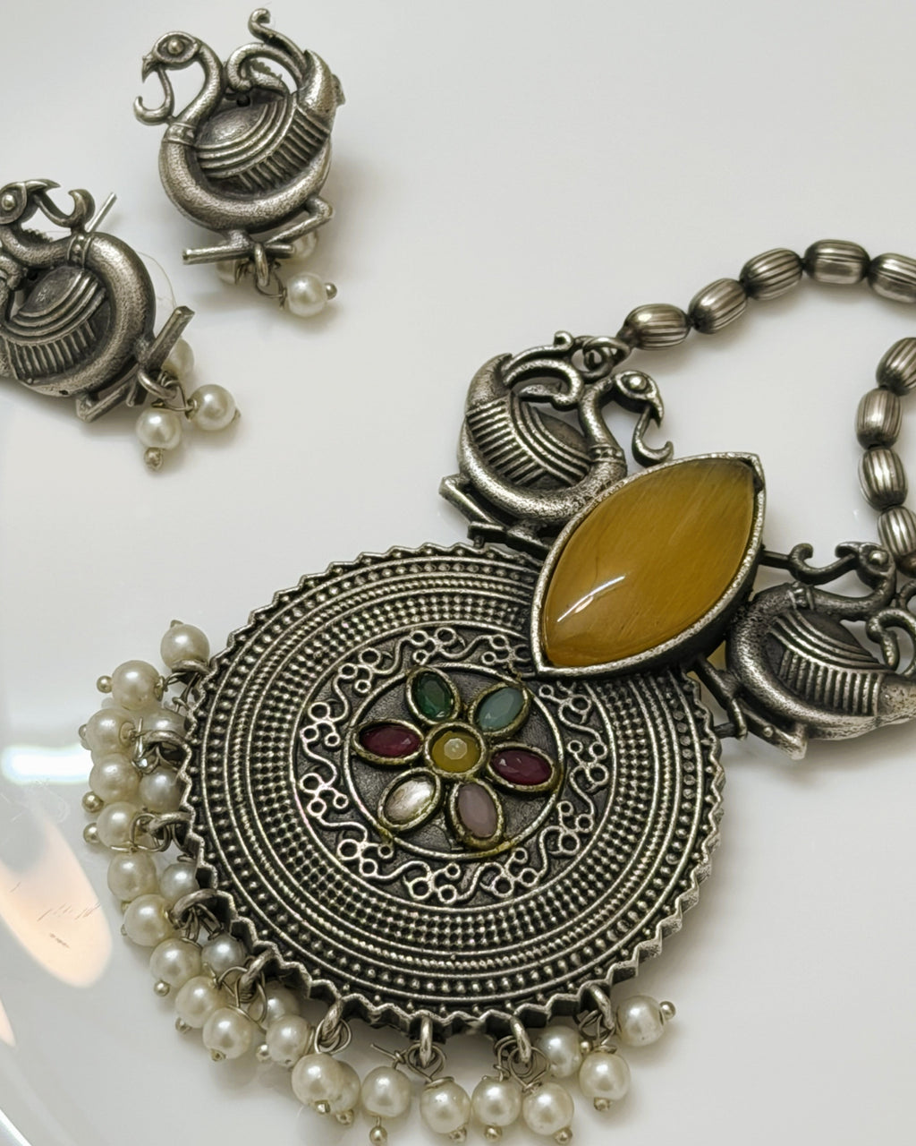 Flat lay of statement ethnic necklace set with peacock motifs, pearl drops and multicolour stones