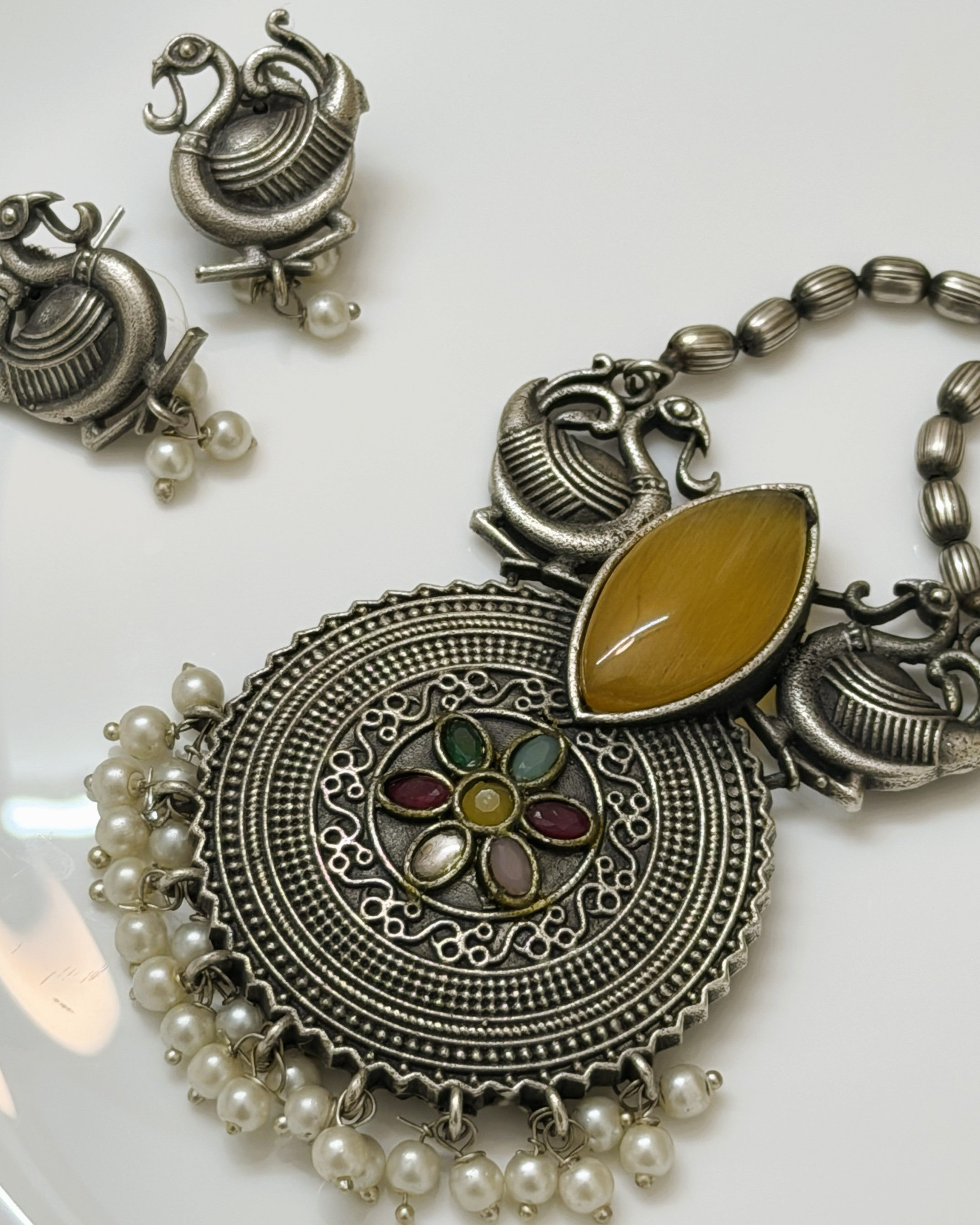 Flat lay of statement ethnic necklace set with peacock motifs, pearl drops and multicolour stones