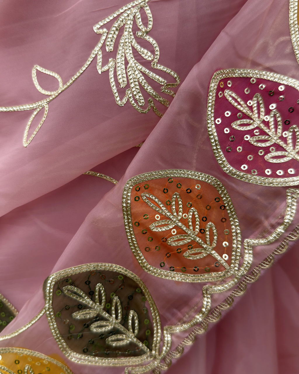 close up of peach organza saree with multicolour leaf motifs and metallic gotta patti work