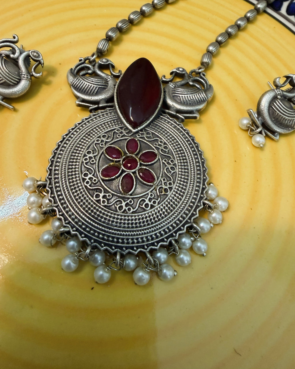 Complete display of necklace and earrings set with red stones, peacock motifs and pearls