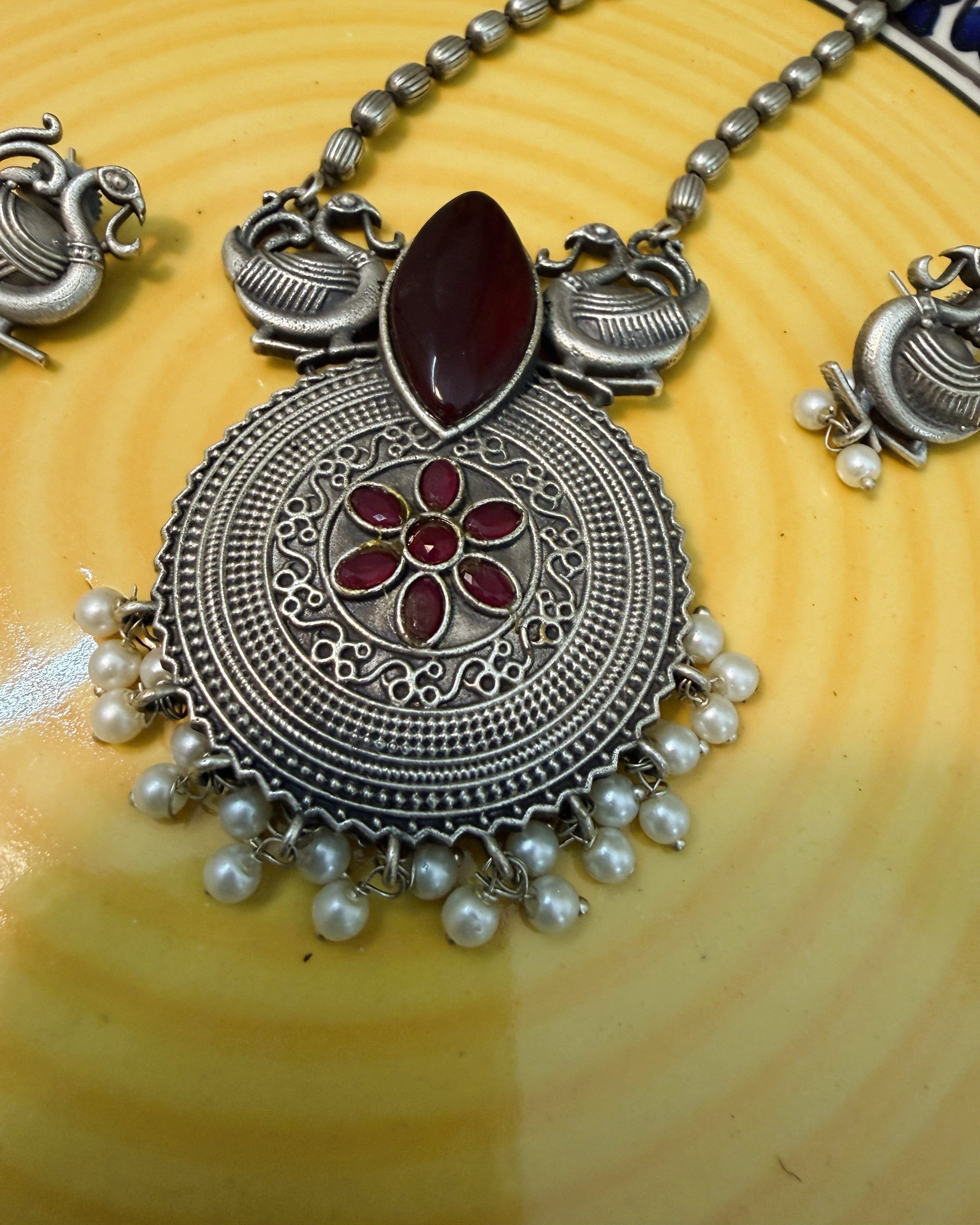 Complete display of necklace and earrings set with red stones, peacock motifs and pearls