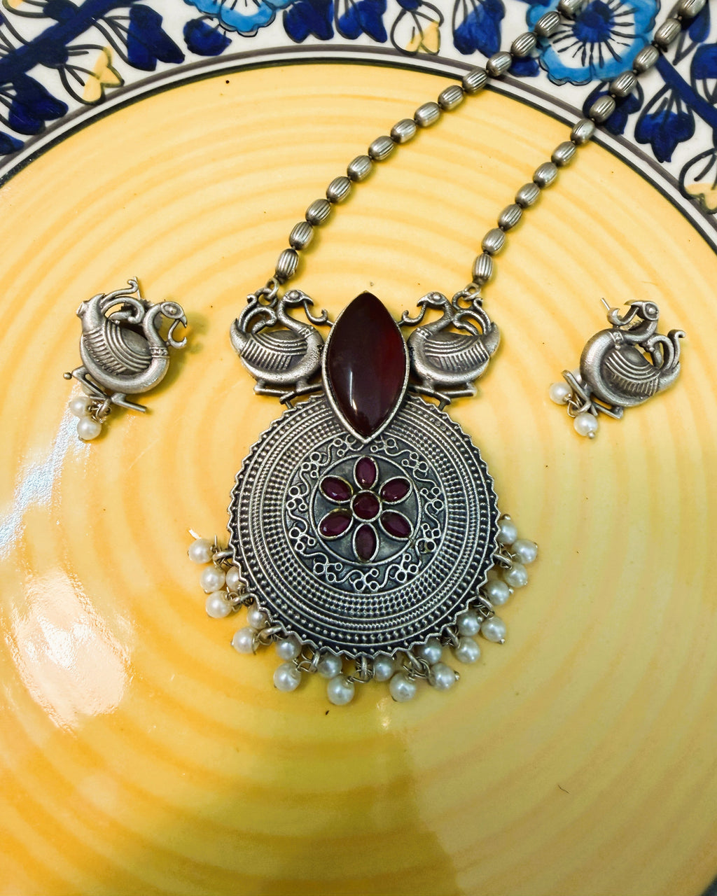 Flat lay of peacock motif necklace set with red stones and pearl drops on neutral background