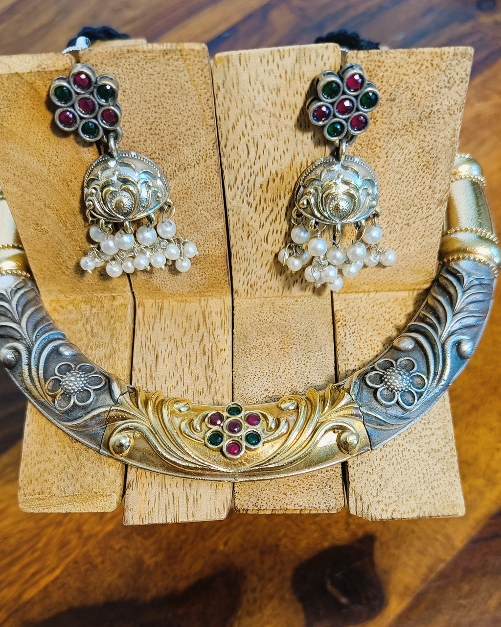 Close-up of dual tone brass choker necklace with intricate floral engraving and gold-tone centrepiece adorned with ruby-red and emerald-green stones