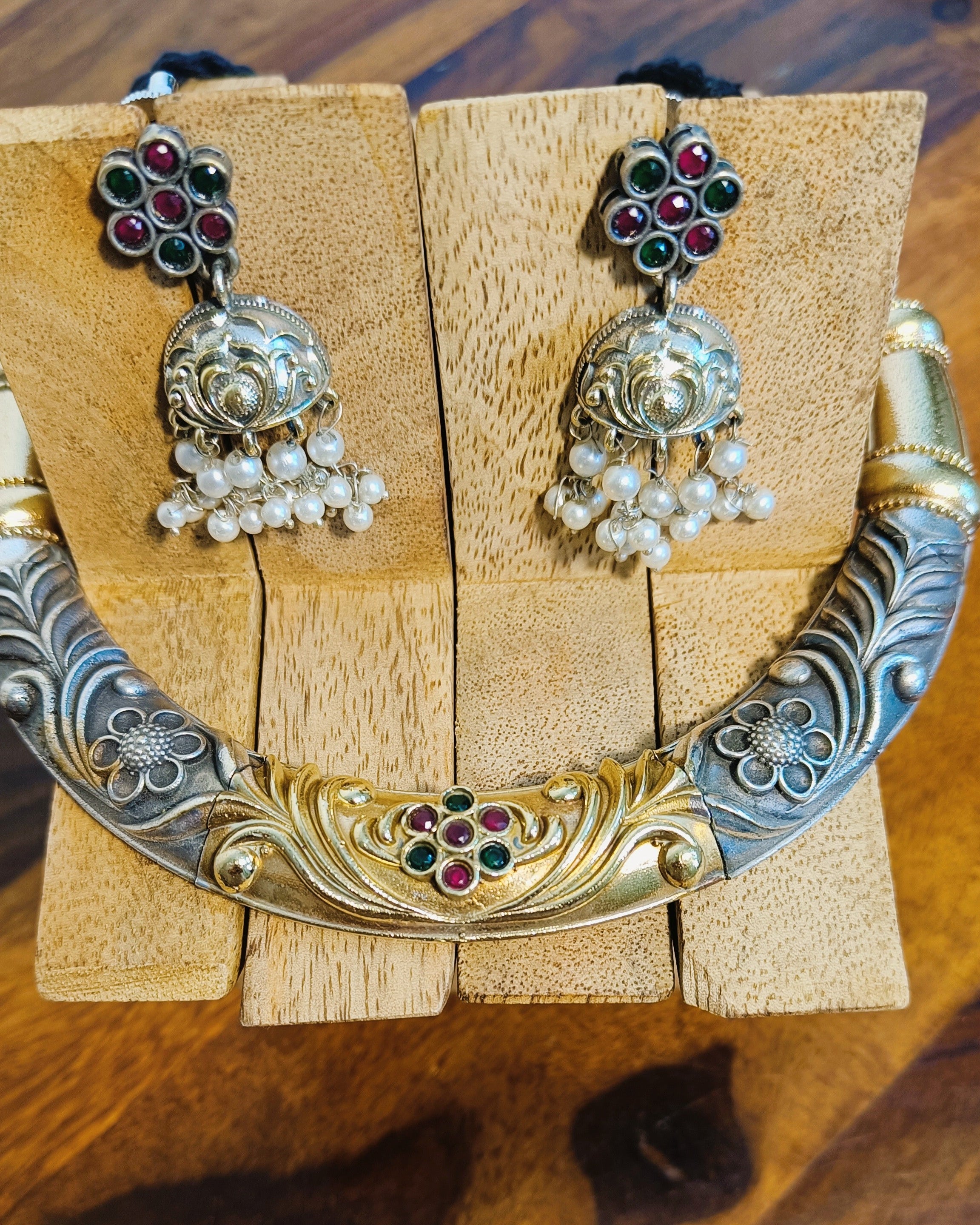 Close-up of dual tone brass choker necklace with intricate floral engraving and gold-tone centrepiece adorned with ruby-red and emerald-green stones