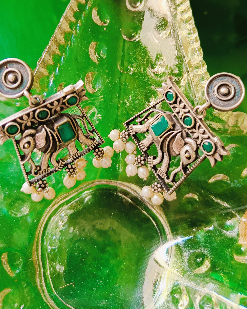 Antique oxidised silver elephant-in-arch stud earrings with emerald-green stone accents and seed pearl drops from the Gajraj Emerald set