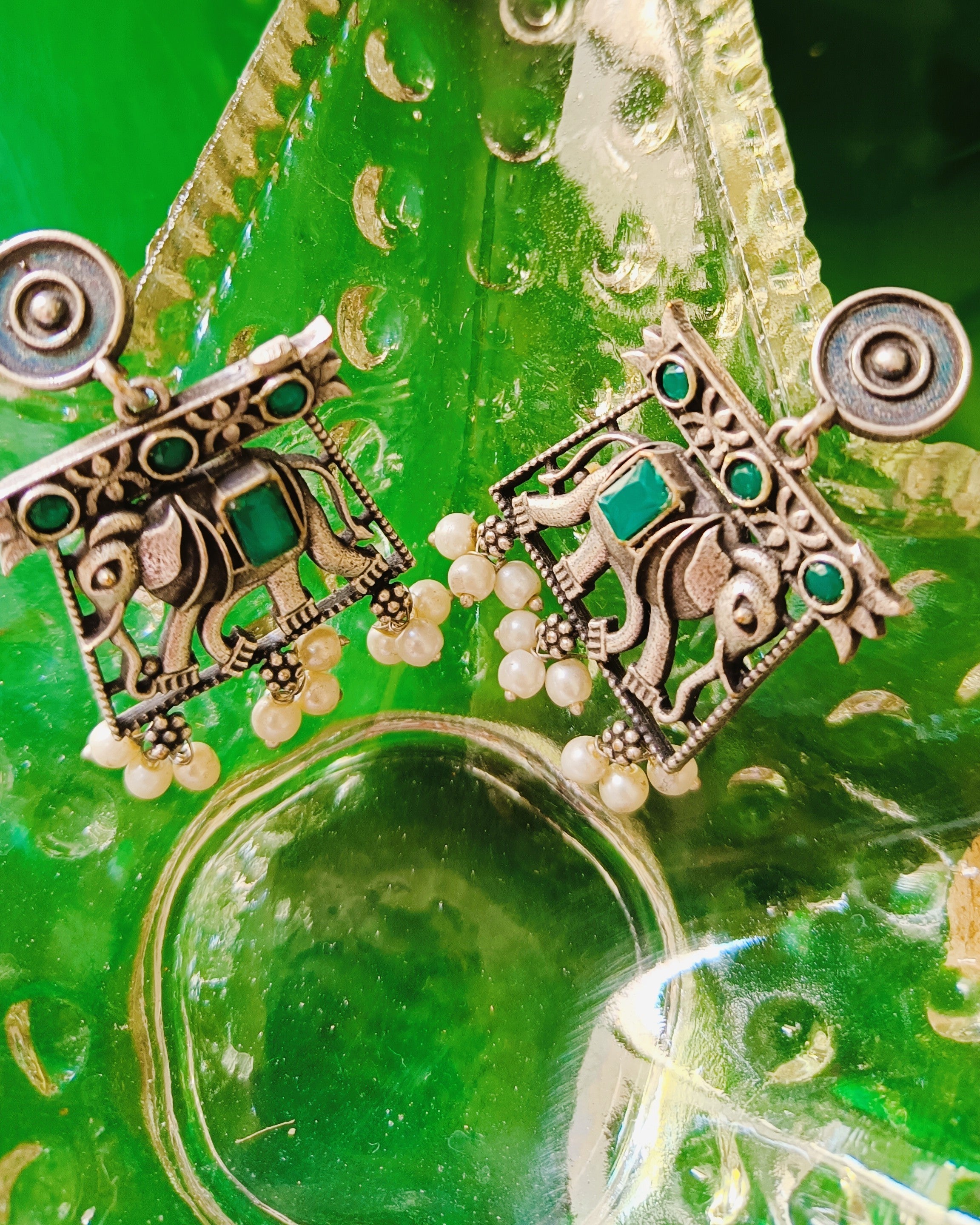 Antique oxidised silver elephant-in-arch stud earrings with emerald-green stone accents and seed pearl drops from the Gajraj Emerald set