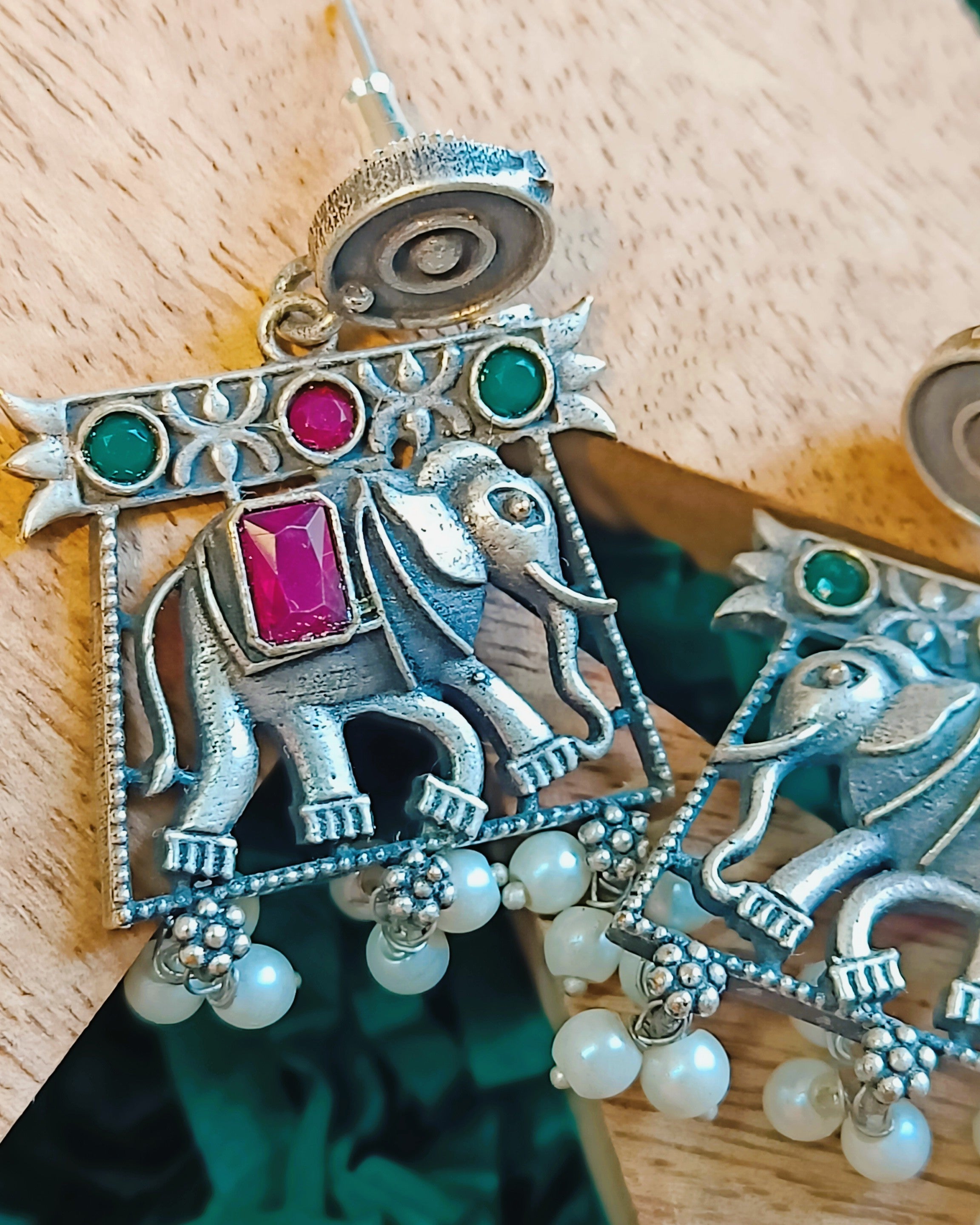 Close-up of oxidised brass elephant motif pendant with ruby-red and emerald-green stones on a ball chain