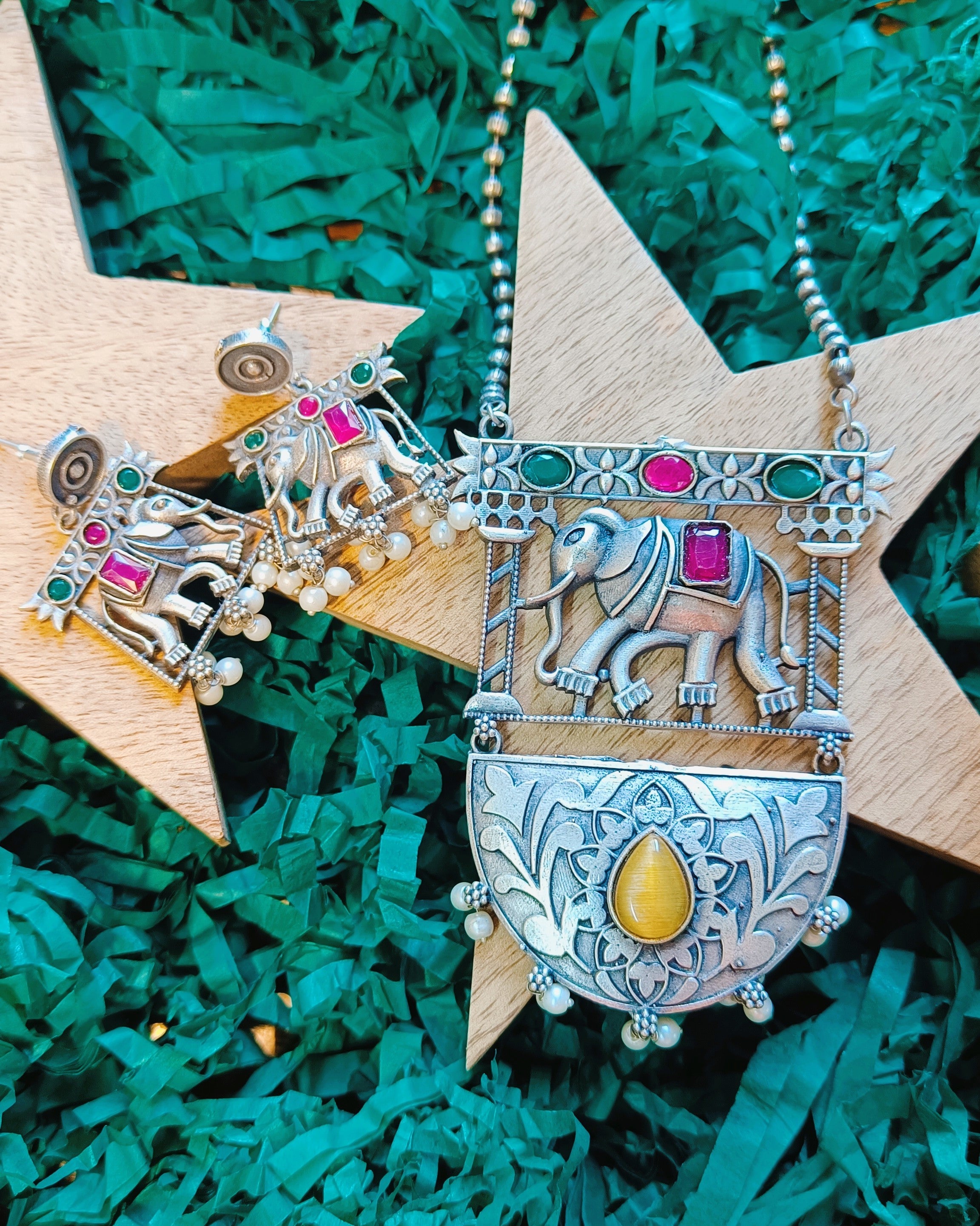 Close-up of oxidised brass elephant motif pendant with ruby-red and emerald-green stones on a ball chain