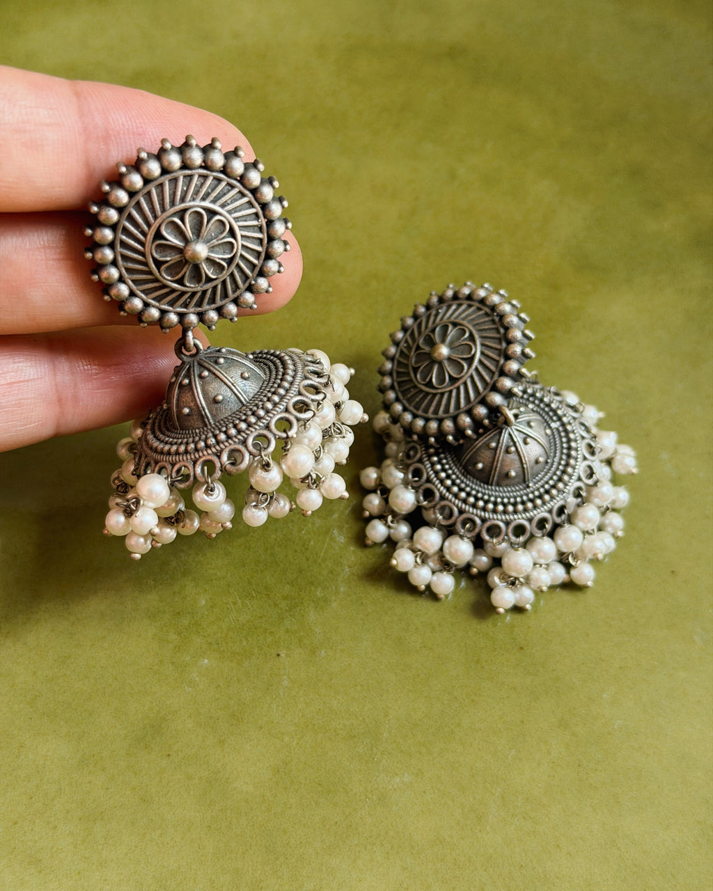 Close-up of the Pushpa jhumka earring held in hand showing the circular floral disc stud with daisy centre motif, ray engraving and raised bead border