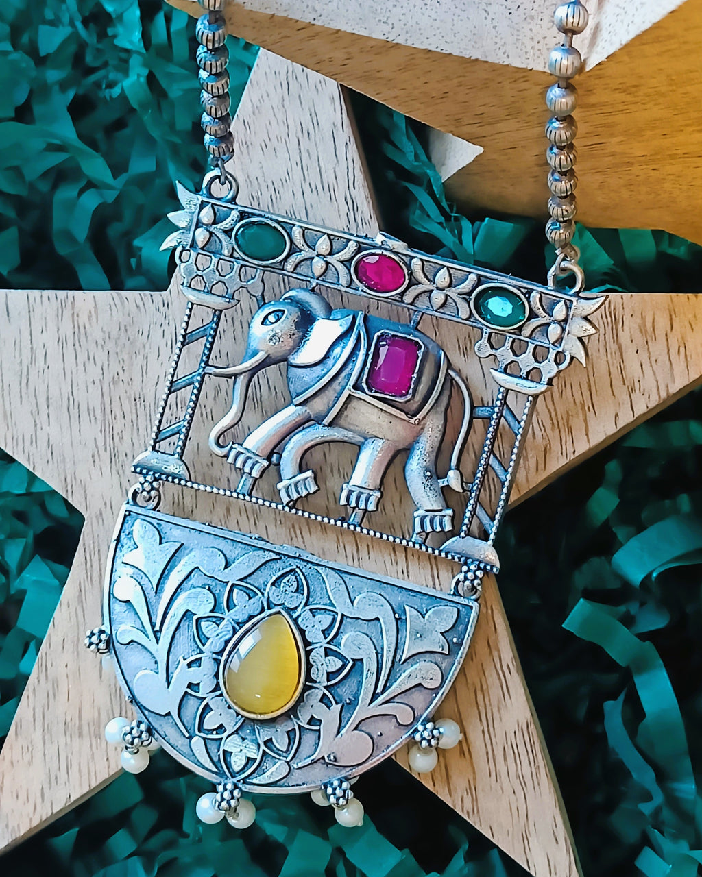 Detailed view of oxidised silver half-moon locket with intricate floral engraving and golden tiger's eye teardrop stone