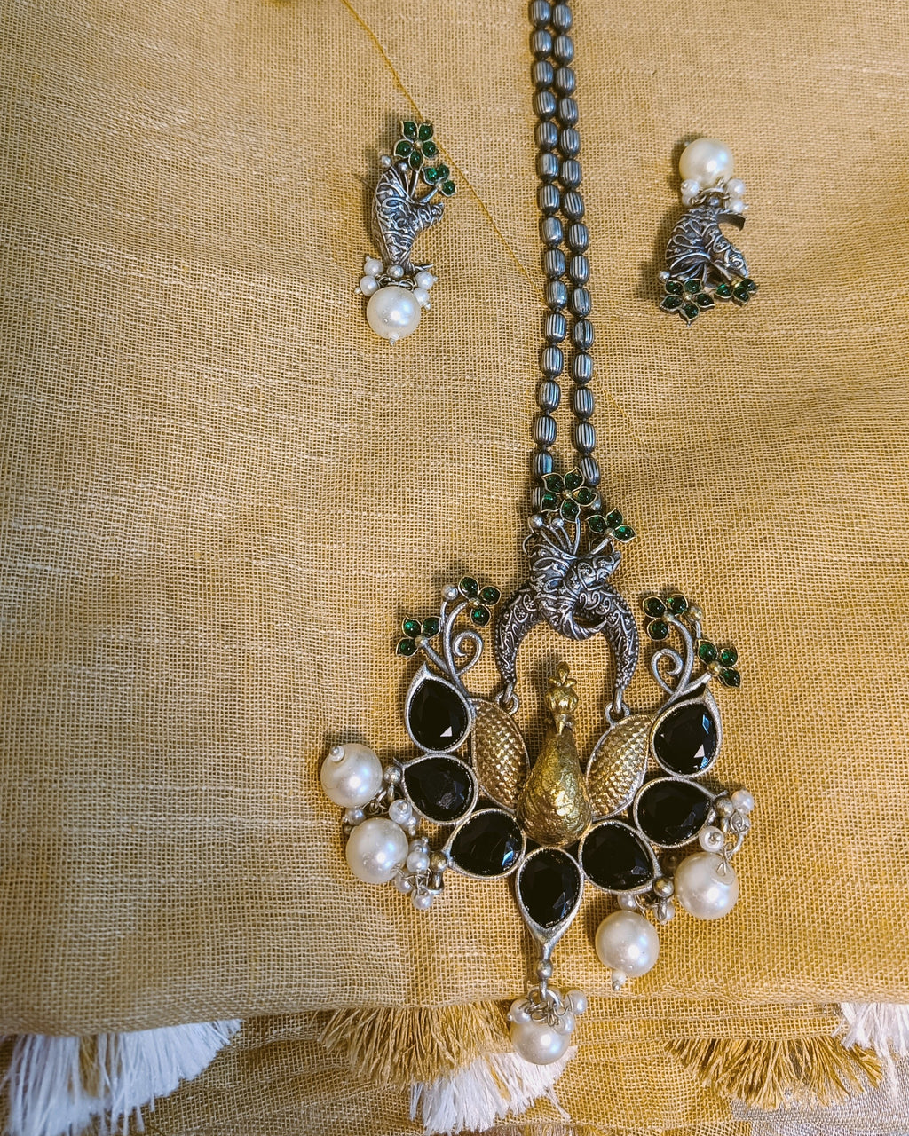 Detailed view of the textured gold-tone locket drop and white pearl cluster at the base of the Mayuri Noir peacock pendant