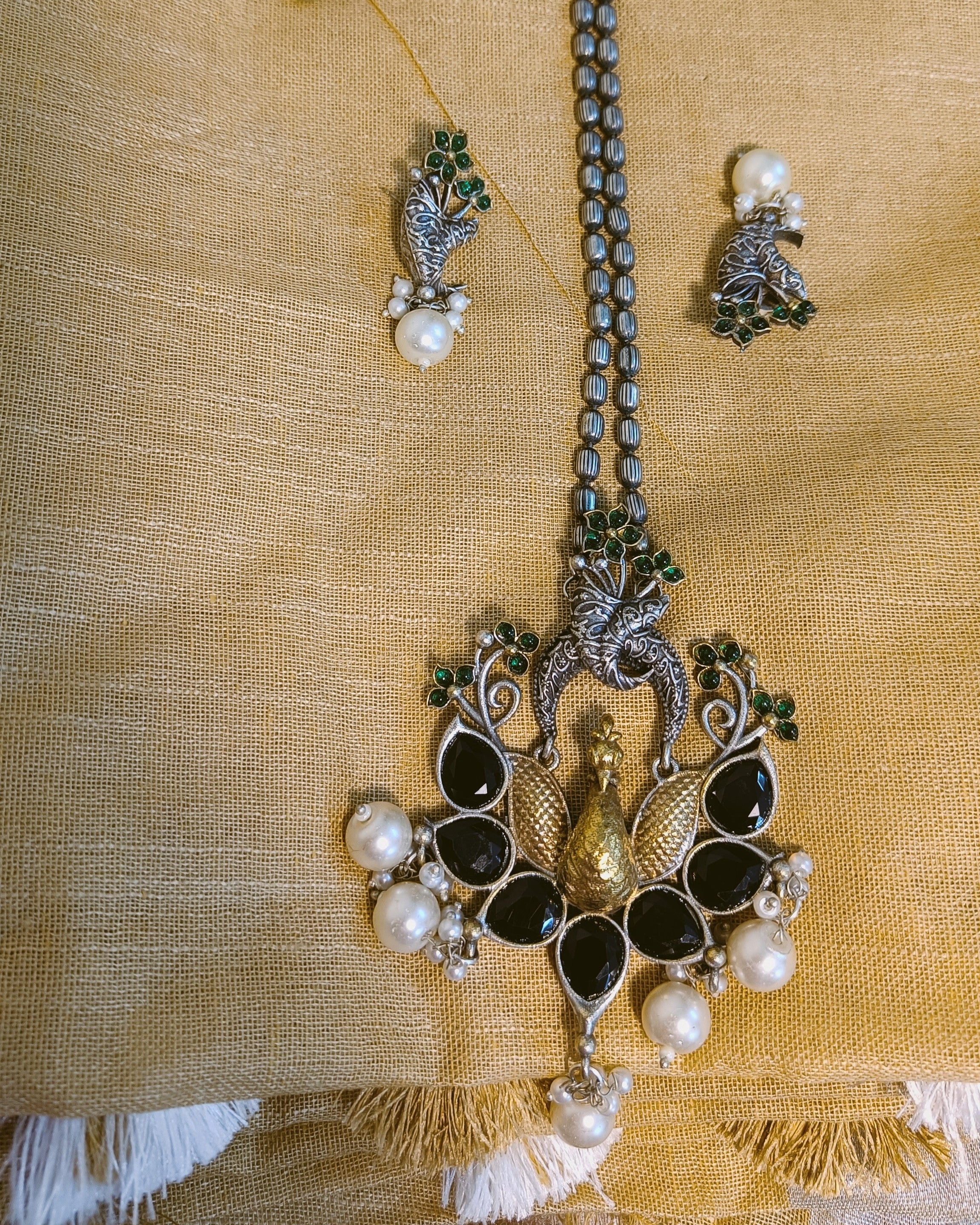 Detailed view of the textured gold-tone locket drop and white pearl cluster at the base of the Mayuri Noir peacock pendant