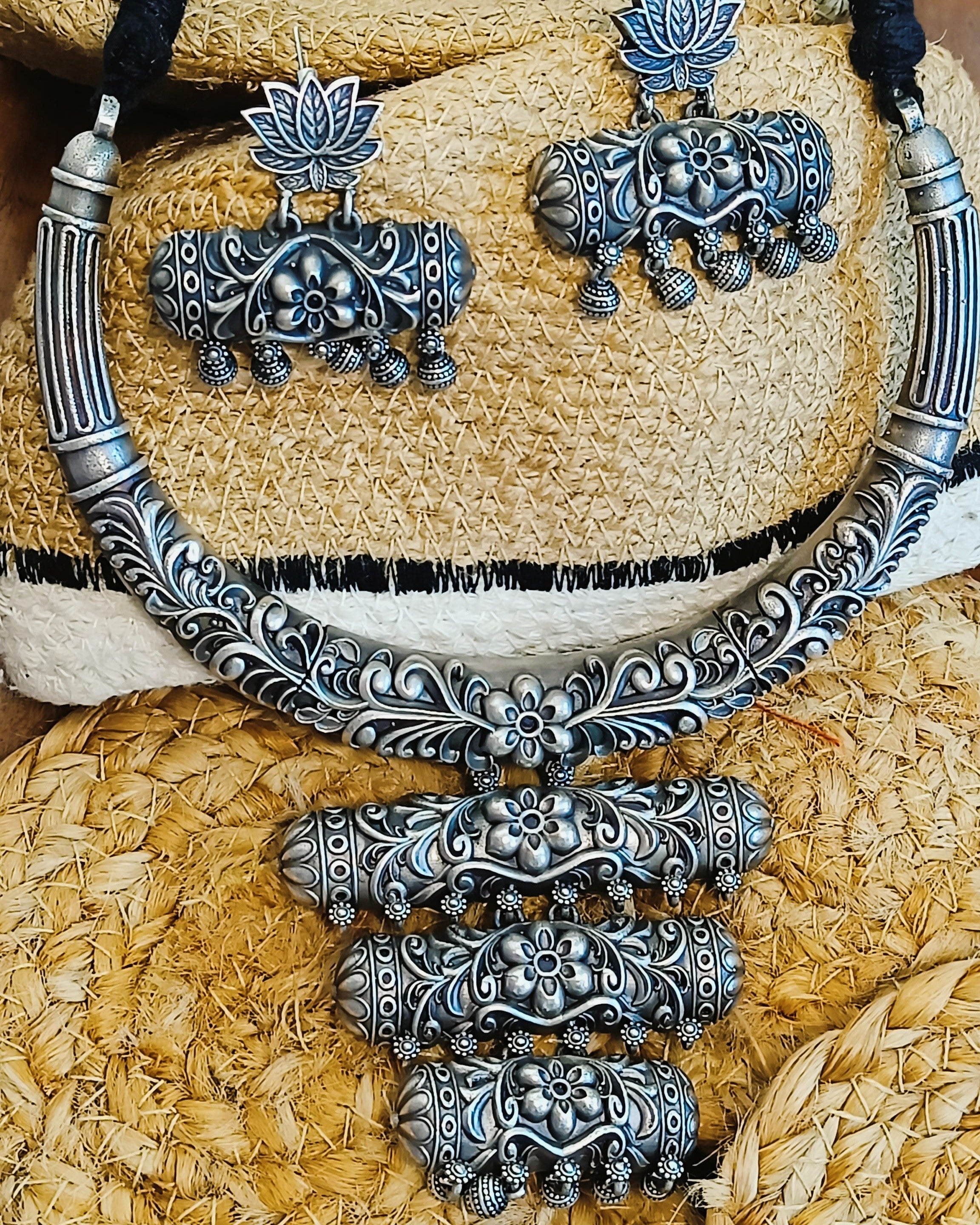 Kamal Vritti antique oxidised silver choker necklace and elephant stud earrings set displayed on a woven hat with black thread cord