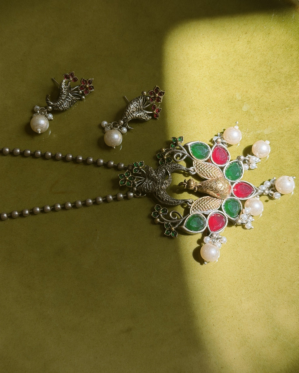 Flatlay of peacock necklace set with earrings on textured background