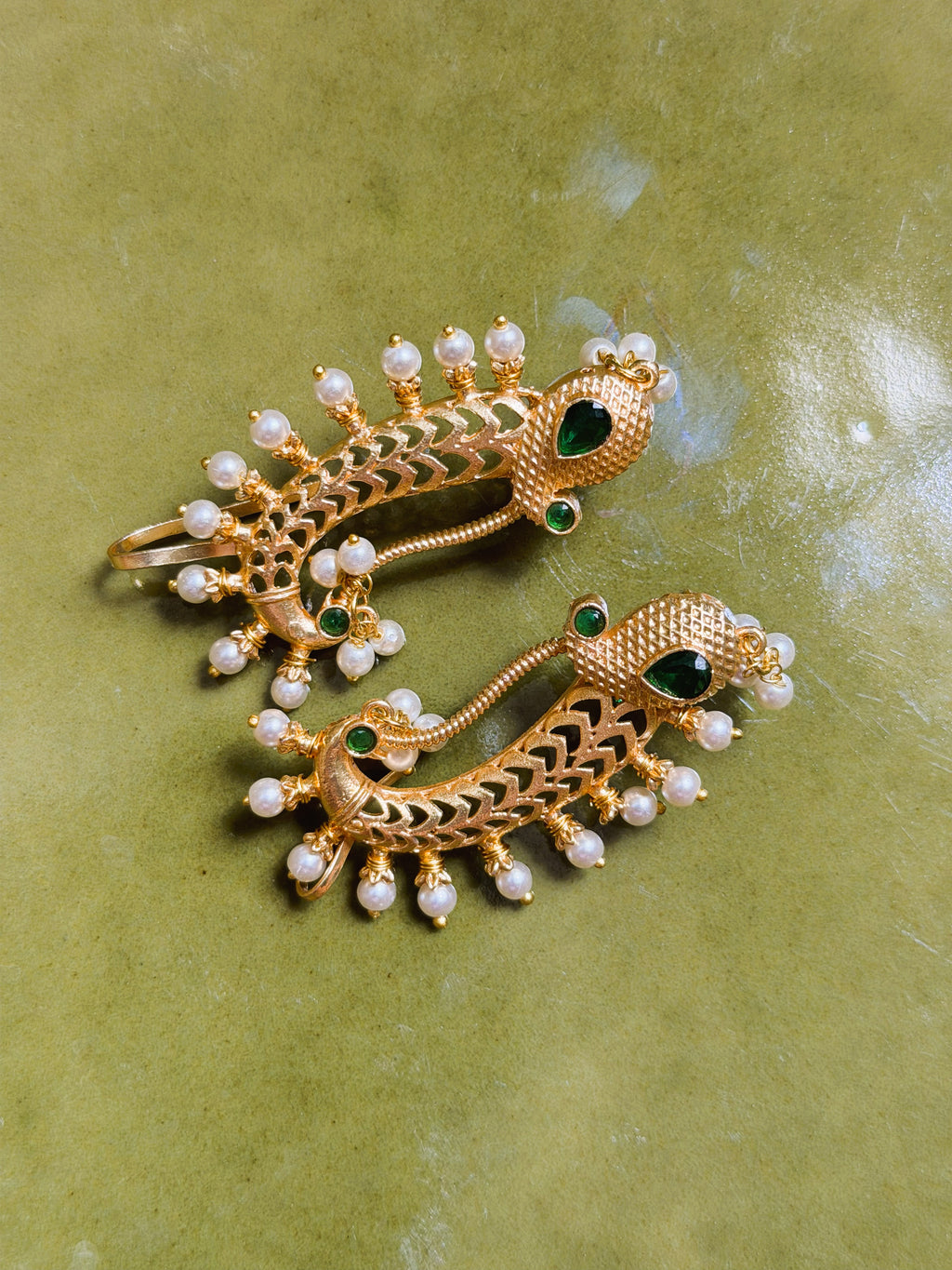 Close-up of peacock motif earrings with textured detailing and green stones