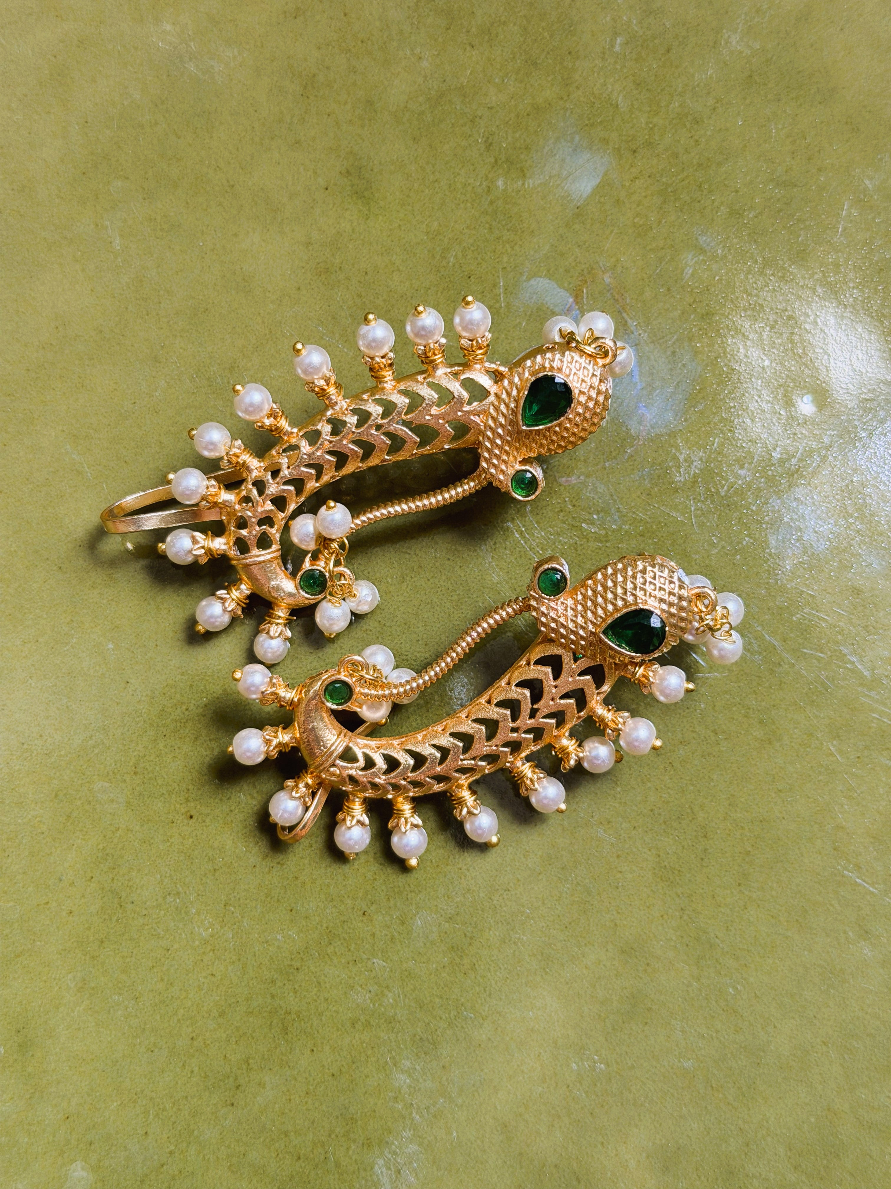 Close-up of peacock motif earrings with textured detailing and green stones