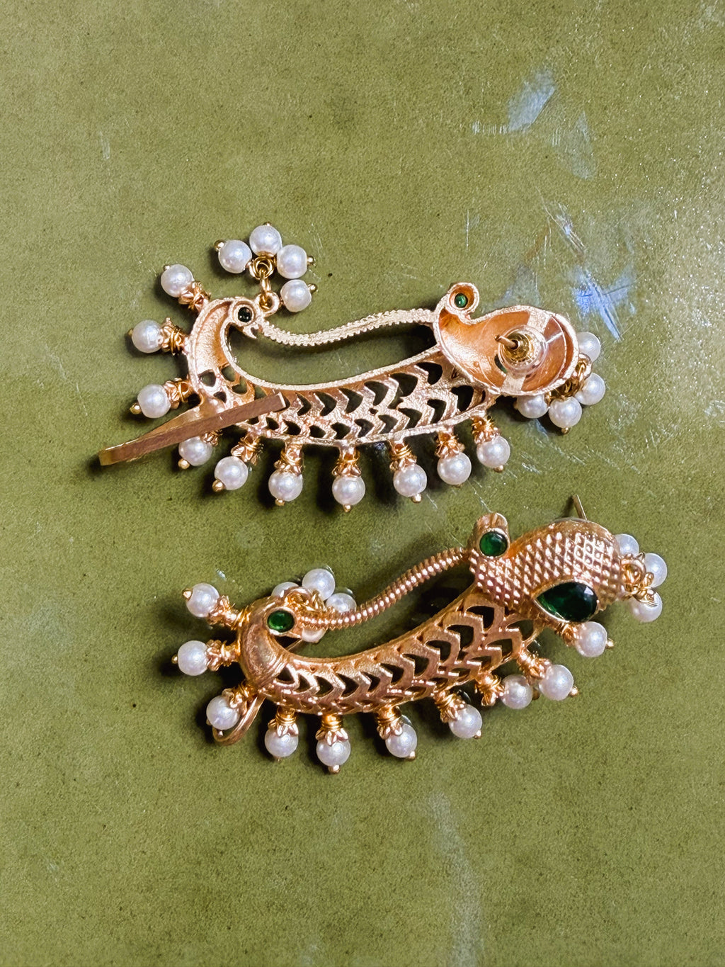 Flatlay of gold peacock earrings on neutral background