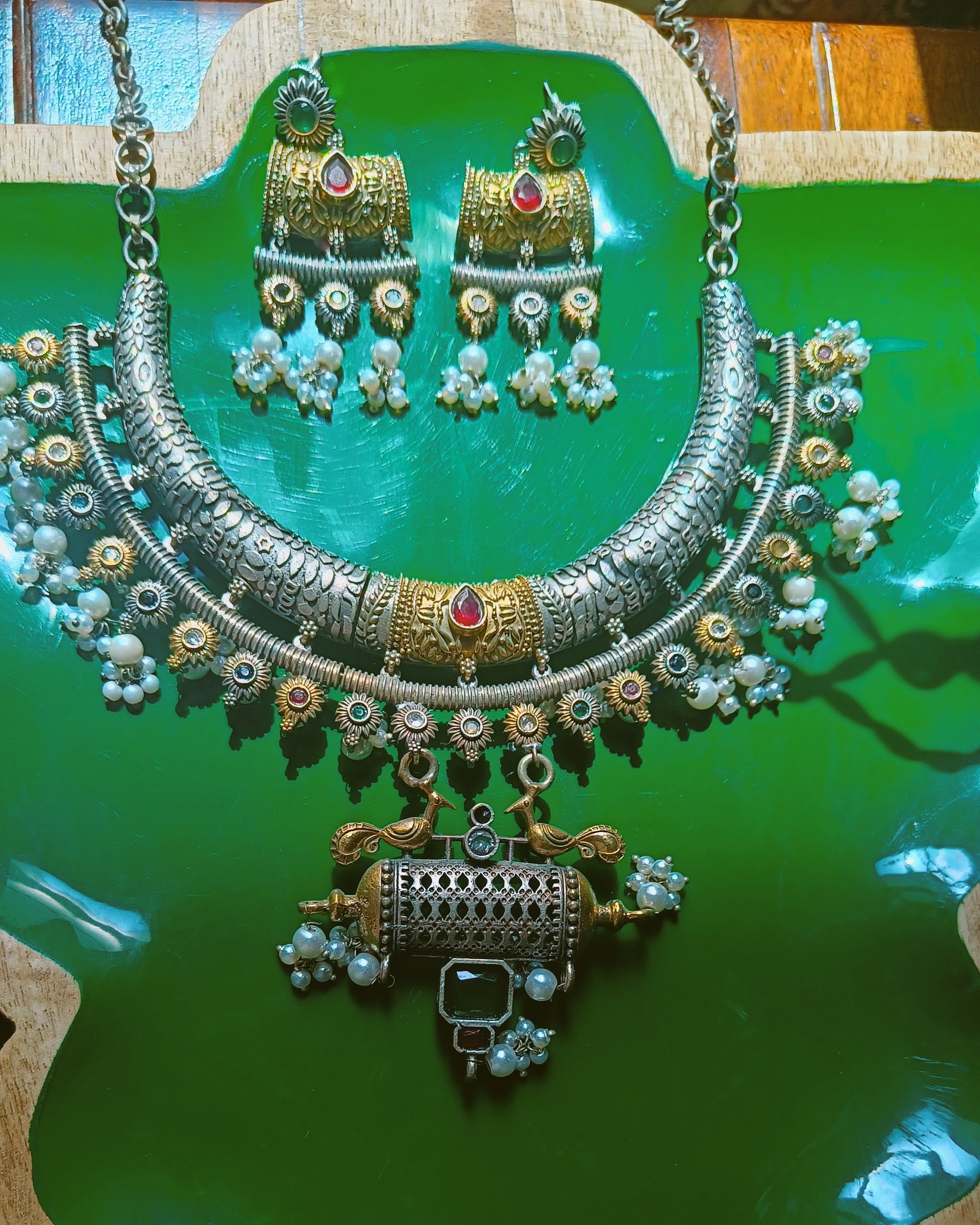 Mughal Baagh dual tone oxidised silver and gold choker necklace and chandelier earrings set displayed on a green wooden jewellery stand