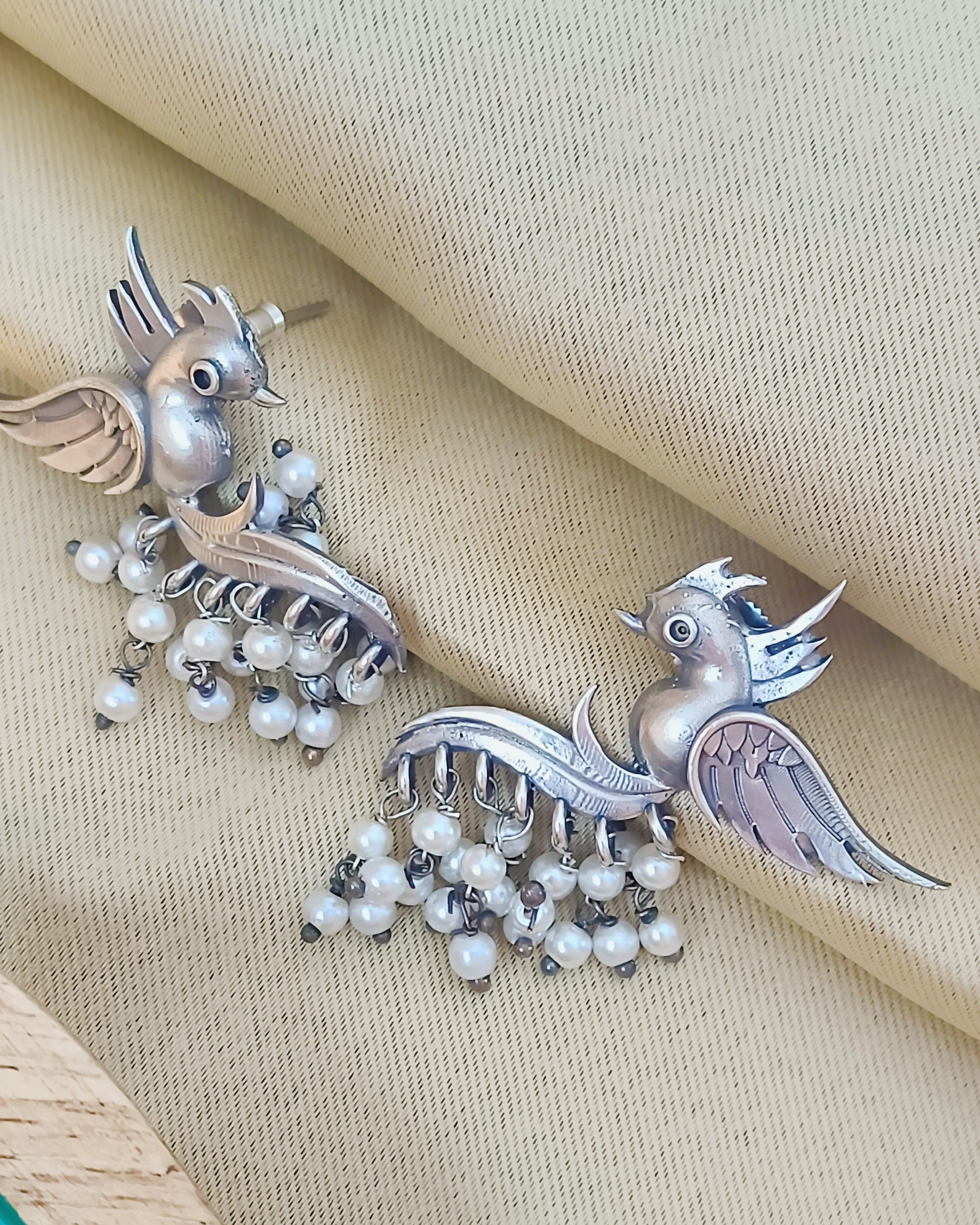 Close-up of bird motif earrings with detailed wings and pearl accents