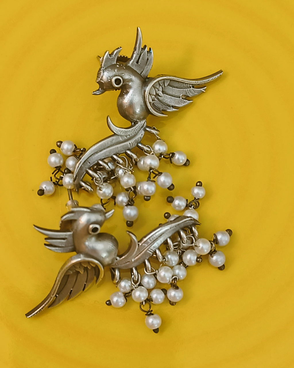 Flatlay of oxidised bird earrings on bright yellow background