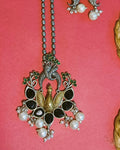 Close-up of oxidised silver peacock pendant with black onyx teardrop stones, emerald-green florals and curling vine detailing