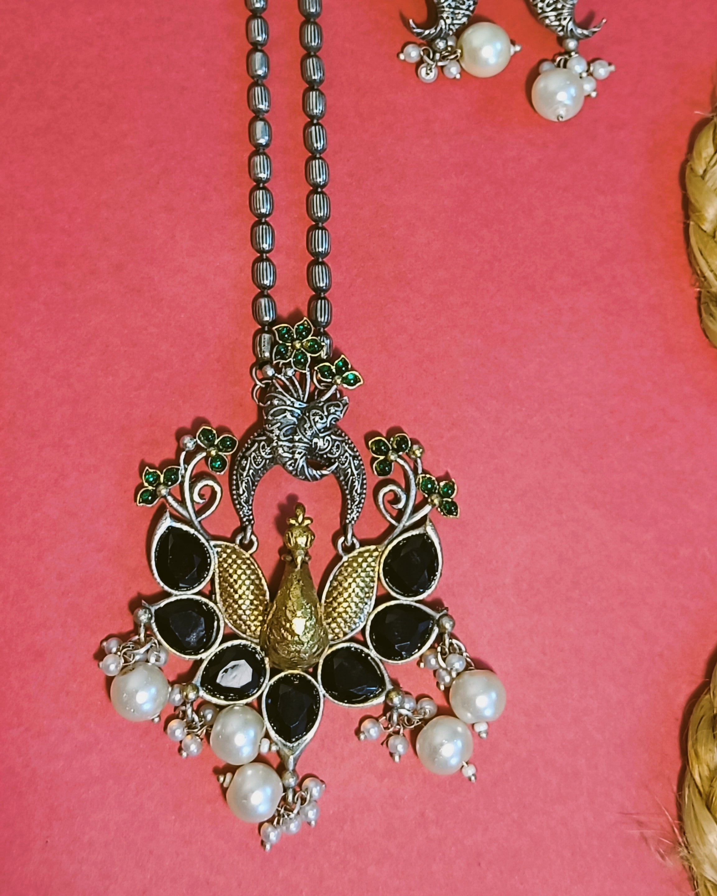 Close-up of oxidised silver peacock pendant with black onyx teardrop stones, emerald-green florals and curling vine detailing