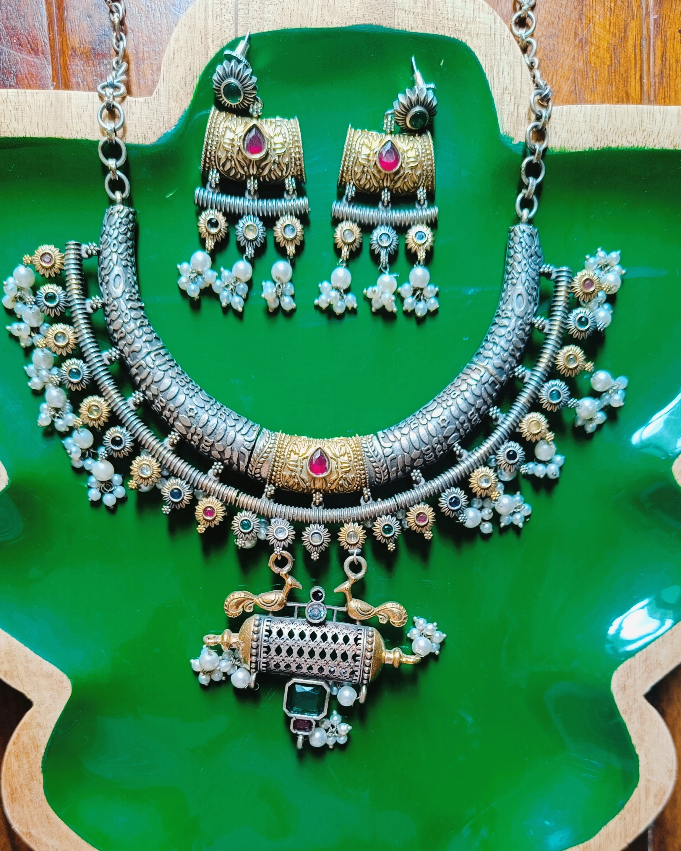 Detailed view of the perforated gold cylinder peacock pendant with emerald-green square stone and pearl drops from the Mughal Baagh necklace set