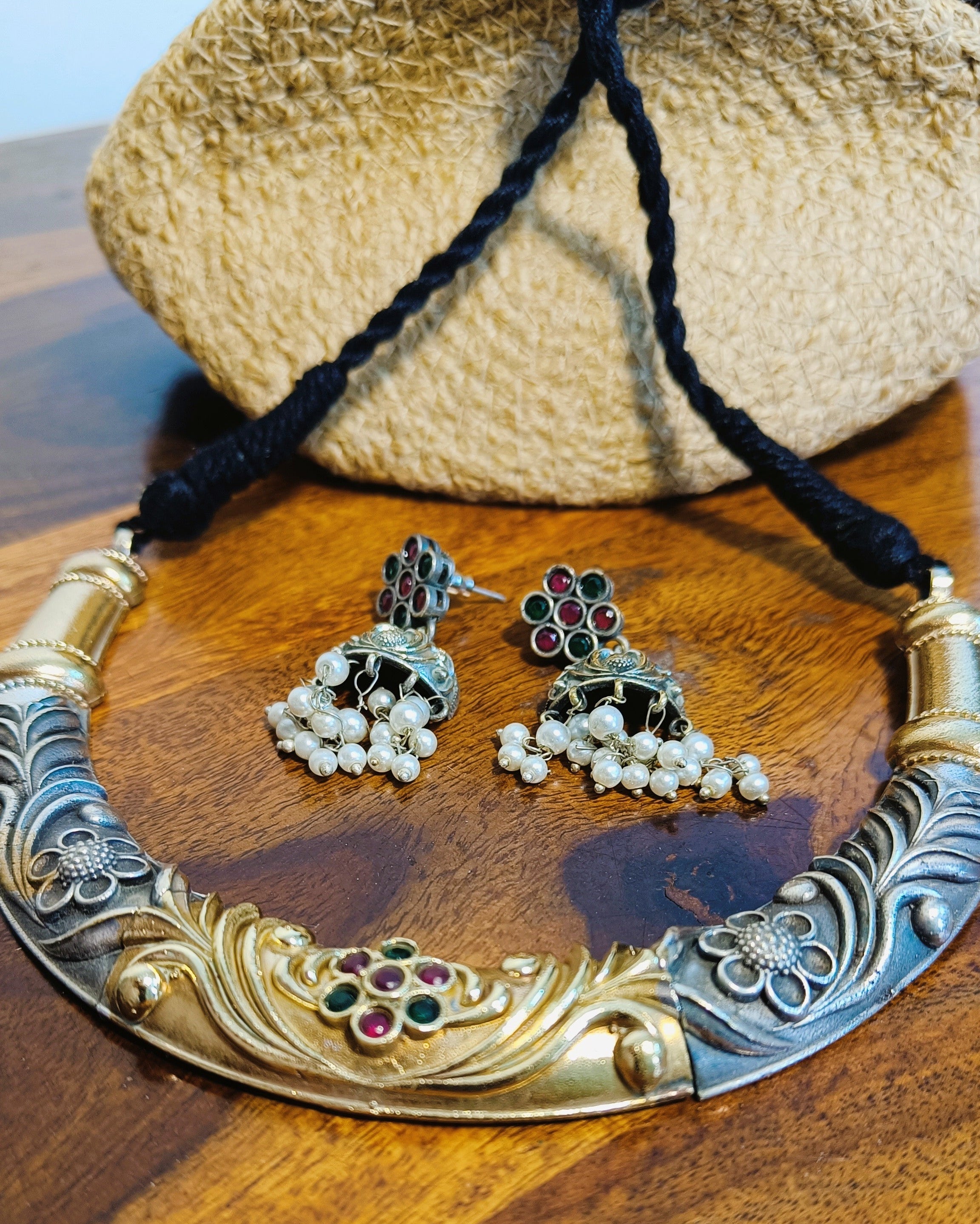 Rajwada dual tone gold and brass choker necklace set with jhumka earrings displayed on a wooden jewellery stand