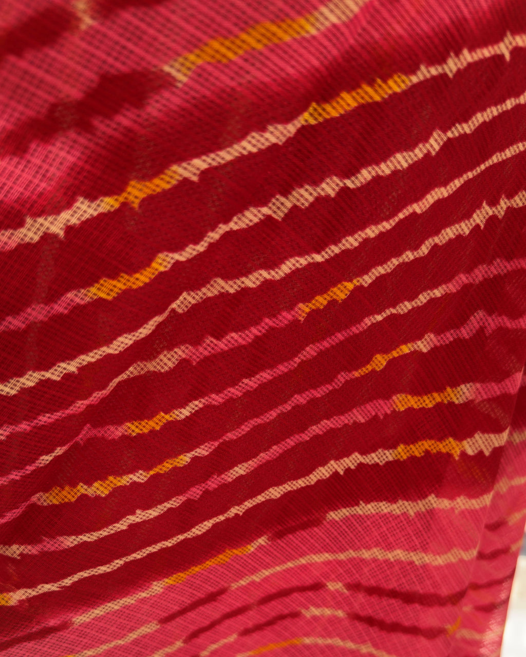 Close-up of diagonal lehriya waves in deep red, pink, and golden yellow on kota doria fabric
