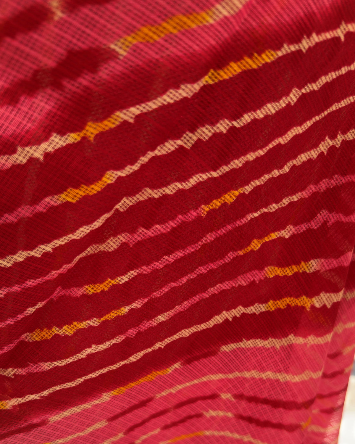 Close-up of diagonal lehriya waves in deep red, pink, and golden yellow on kota doria fabric
