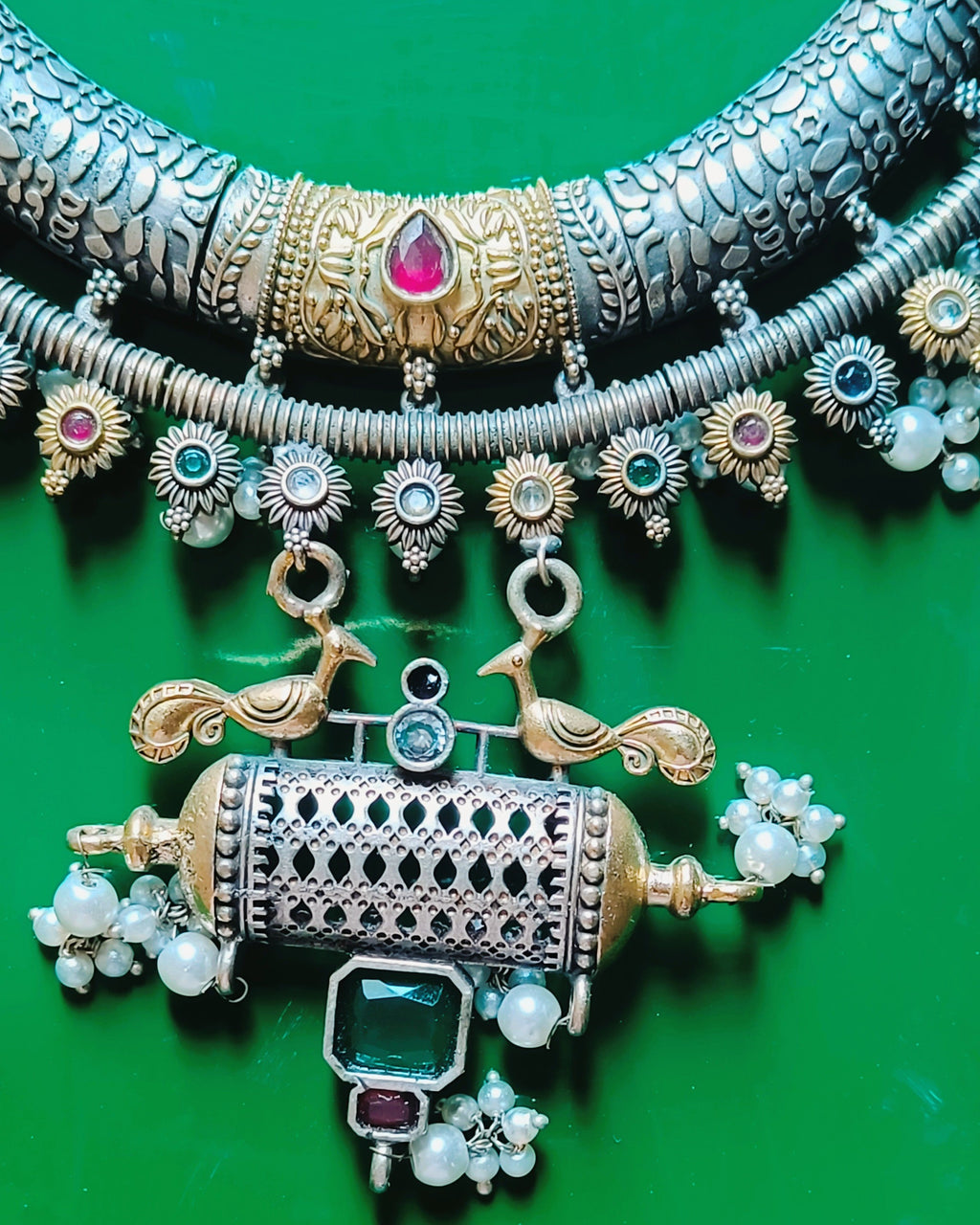 Close-up of Mughal Baagh scale-textured oxidised silver crescent choker with gold centrepieces, ruby-red stones and sunflower border with pearl drops
