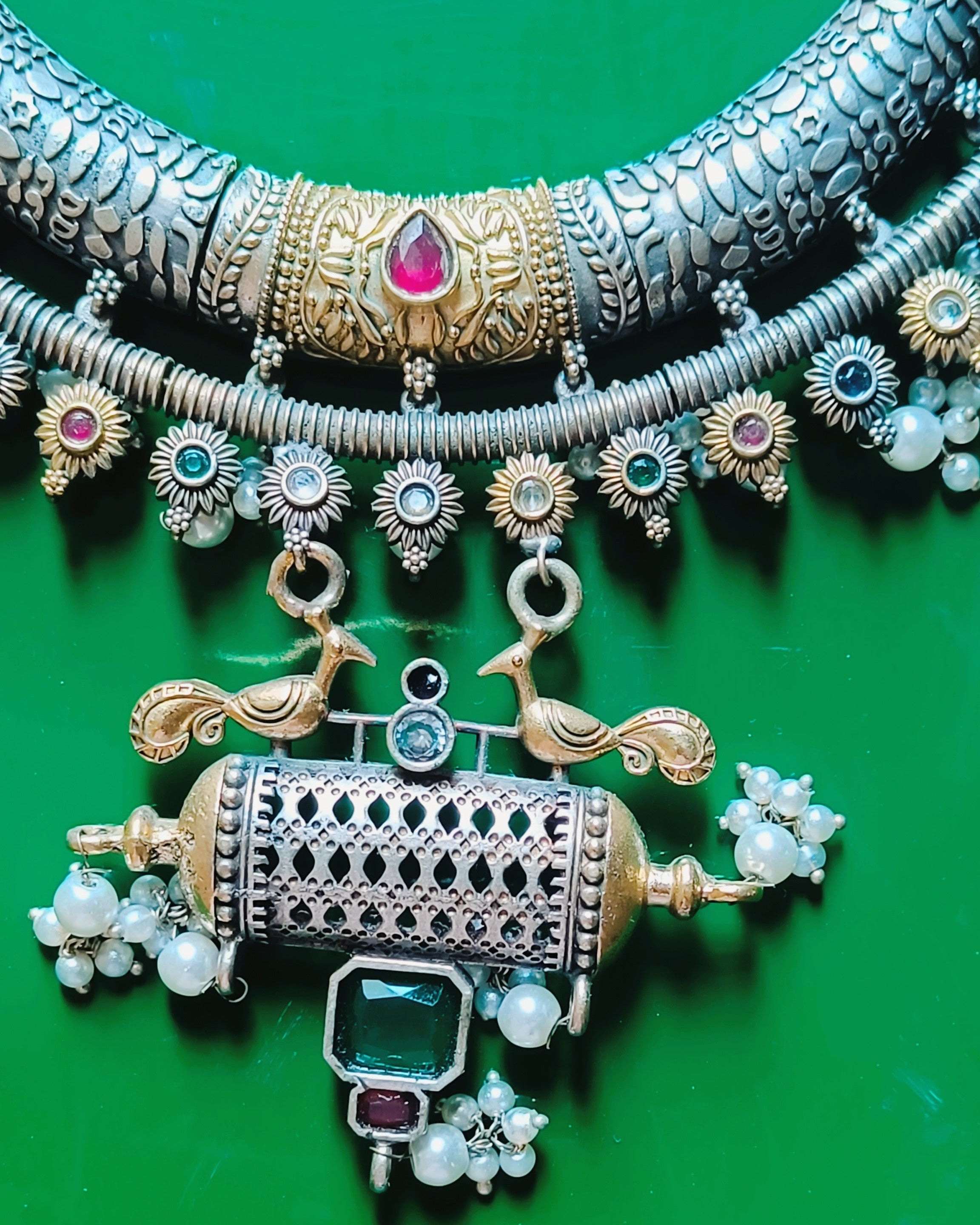 Close-up of Mughal Baagh scale-textured oxidised silver crescent choker with gold centrepieces, ruby-red stones and sunflower border with pearl drops