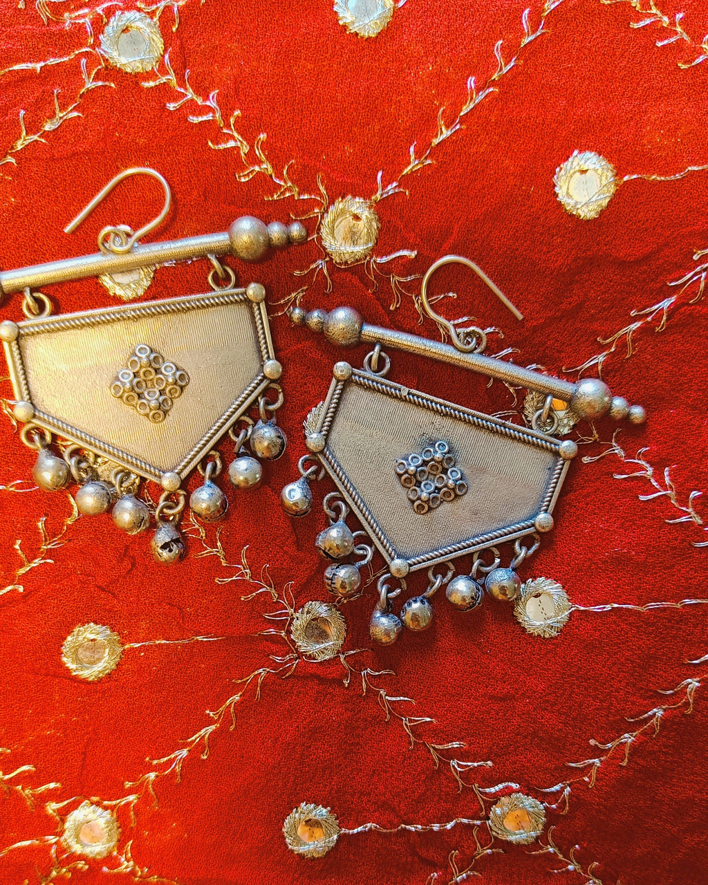 Close-up of antique oxidised silver shield-shaped earring with twisted rope border and raised diamond lattice centre motif