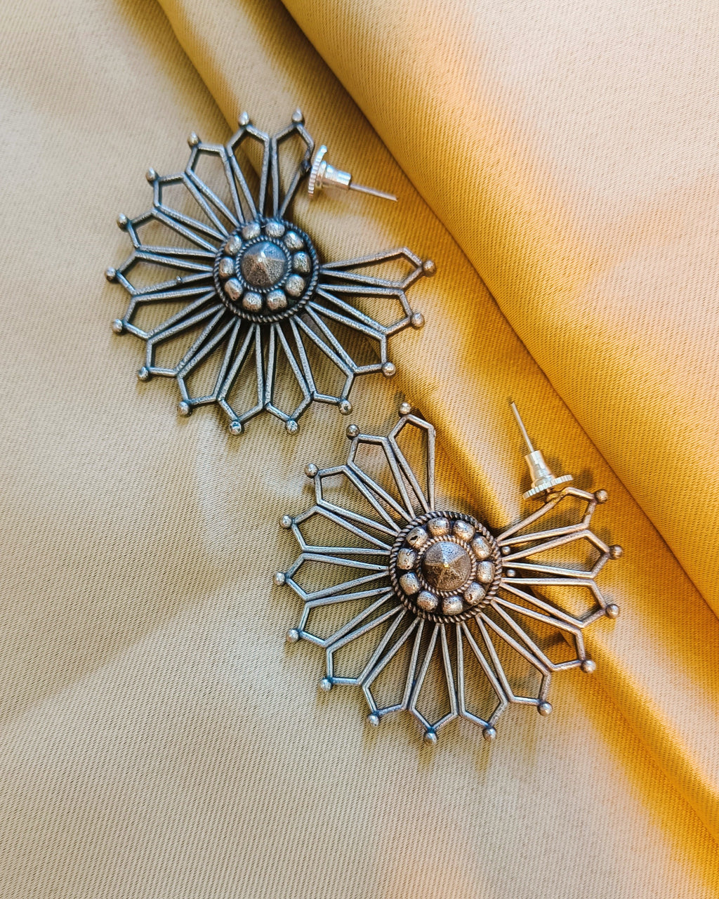 Close-up of a single Surya Chakra antique oxidised silver sunburst stud earring showing the open-work geometric rays and hexagonal tip frames