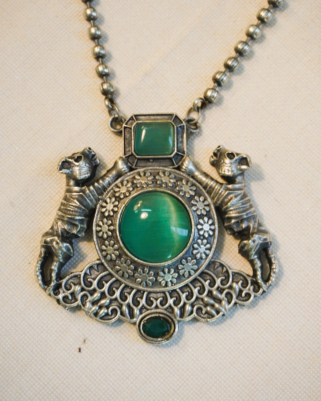 Close-up of antique oxidised silver twin lion pendant with large round green onyx cabochon stone set within a floral-engraved medallion