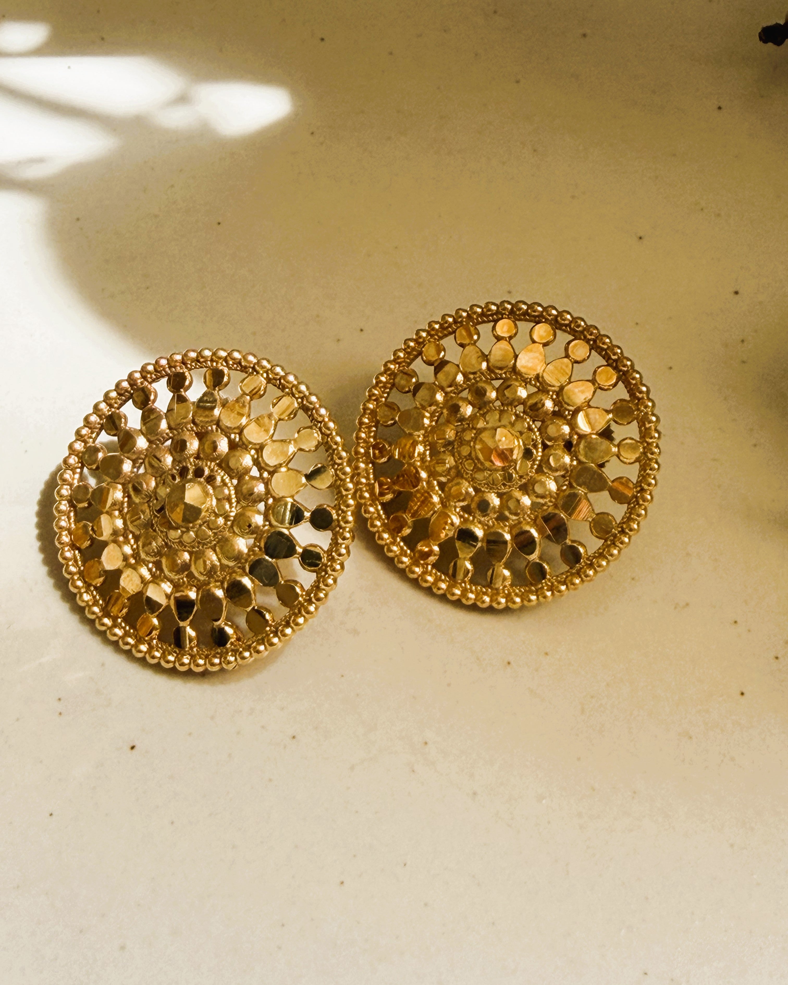 Close-up of gold stud earrings with petal pattern and beaded border